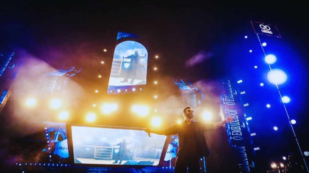 Gusttavo Lima em palco iluminado com telões, representando a transição entre o sertanejo universitário e o agronejo moderno.
