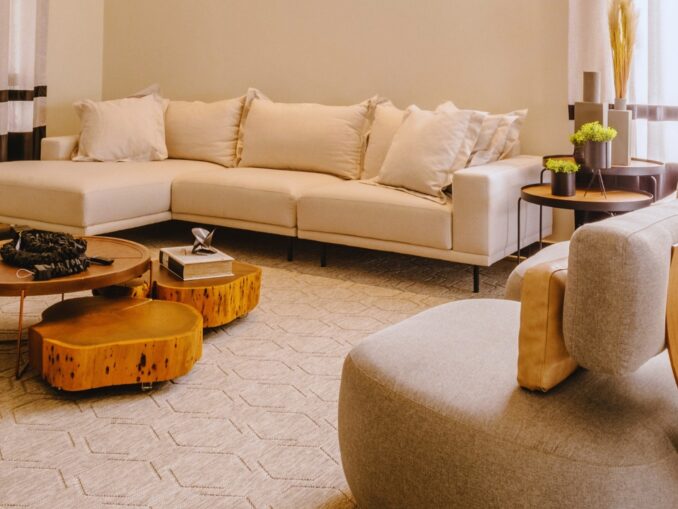 Sala de estar moderna com sofá bege e mesas de centro em madeira clara, sob luz natural