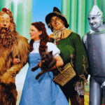 Cena do filme The Wizard of Oz (1939) mostrando Dorothy, o Espantalho, o Homem de Lata e o Leão Covarde em cores vibrantes do Technicolor.